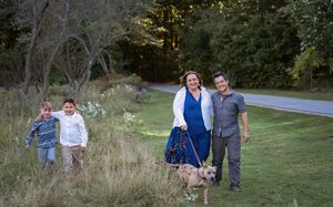 Family with two boys and dog posing on grassy path surrounded by trees.