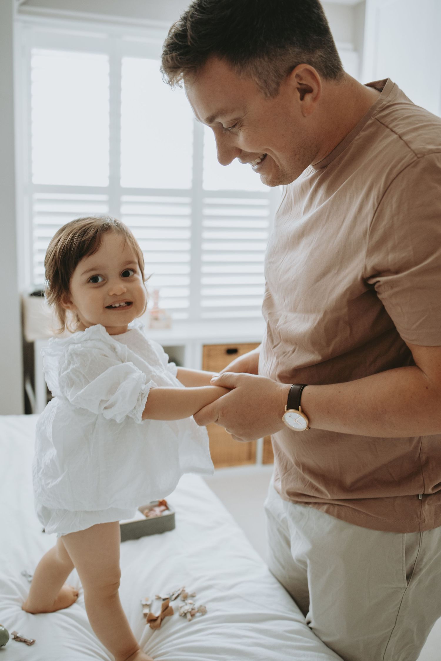 Sweet interactions between parent and child on a white bed in a sunlit room.