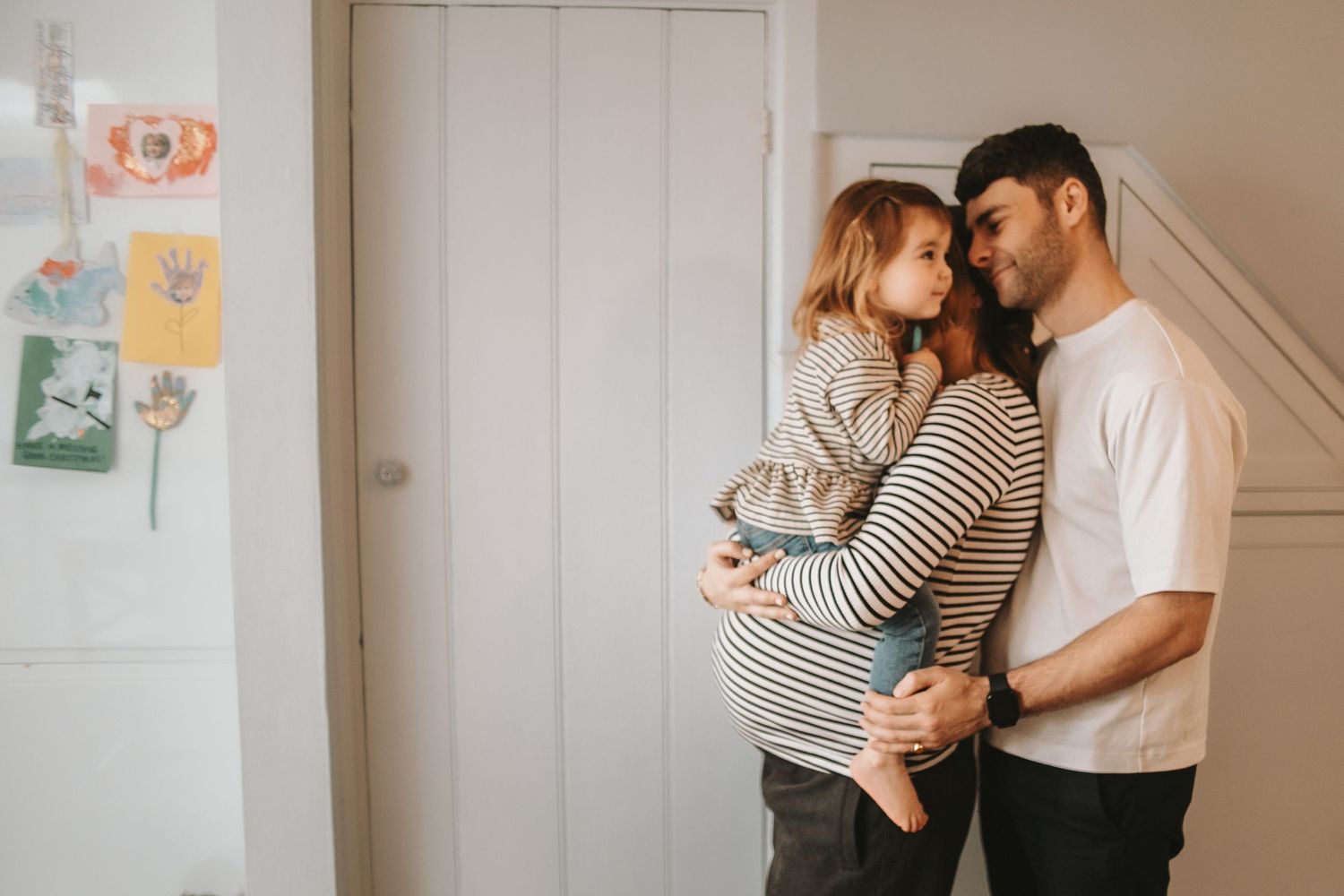 Family sharing tender moment together against white wall with child artwork.