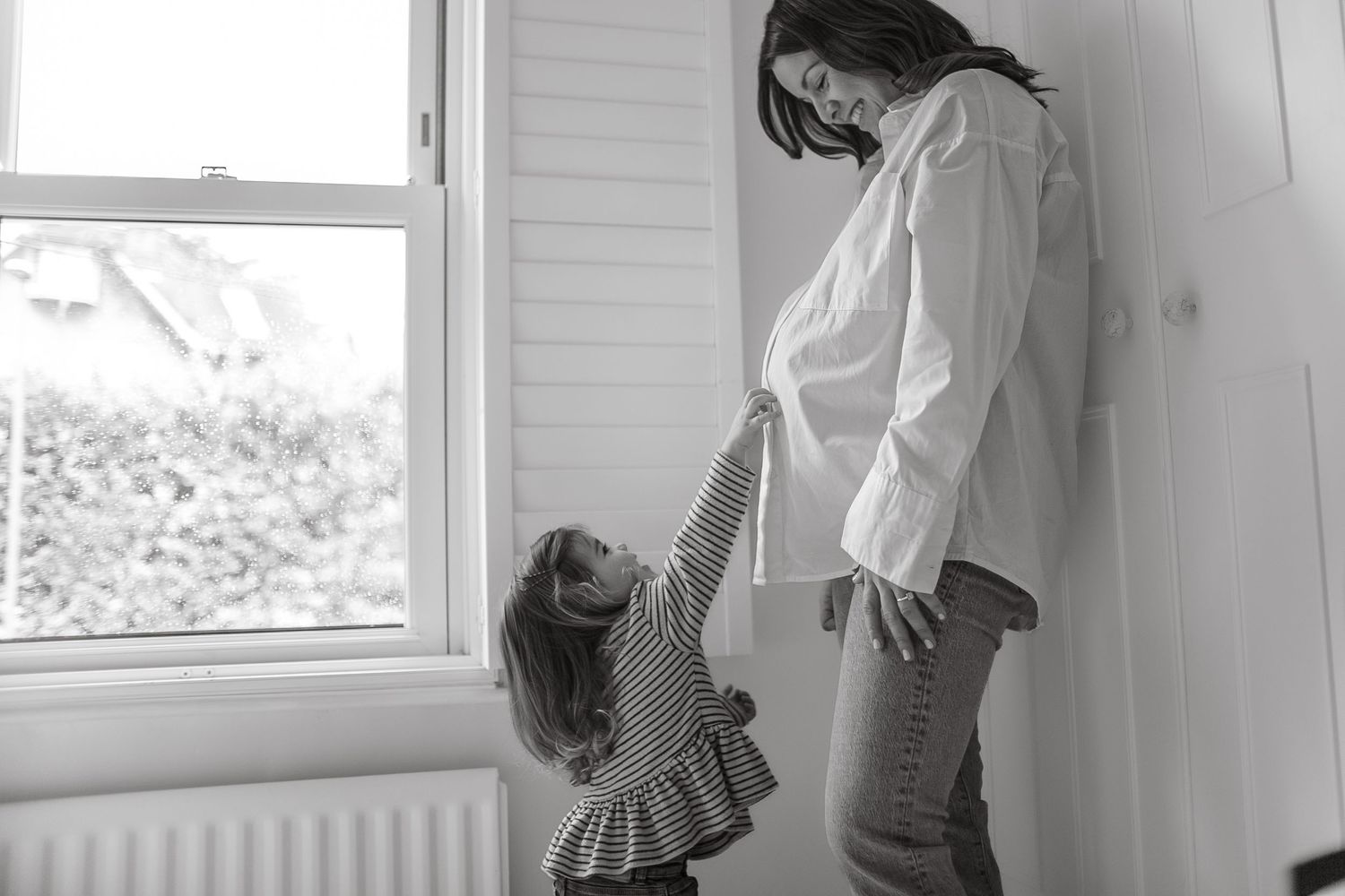 Black and white image of parent and child interacting by window.