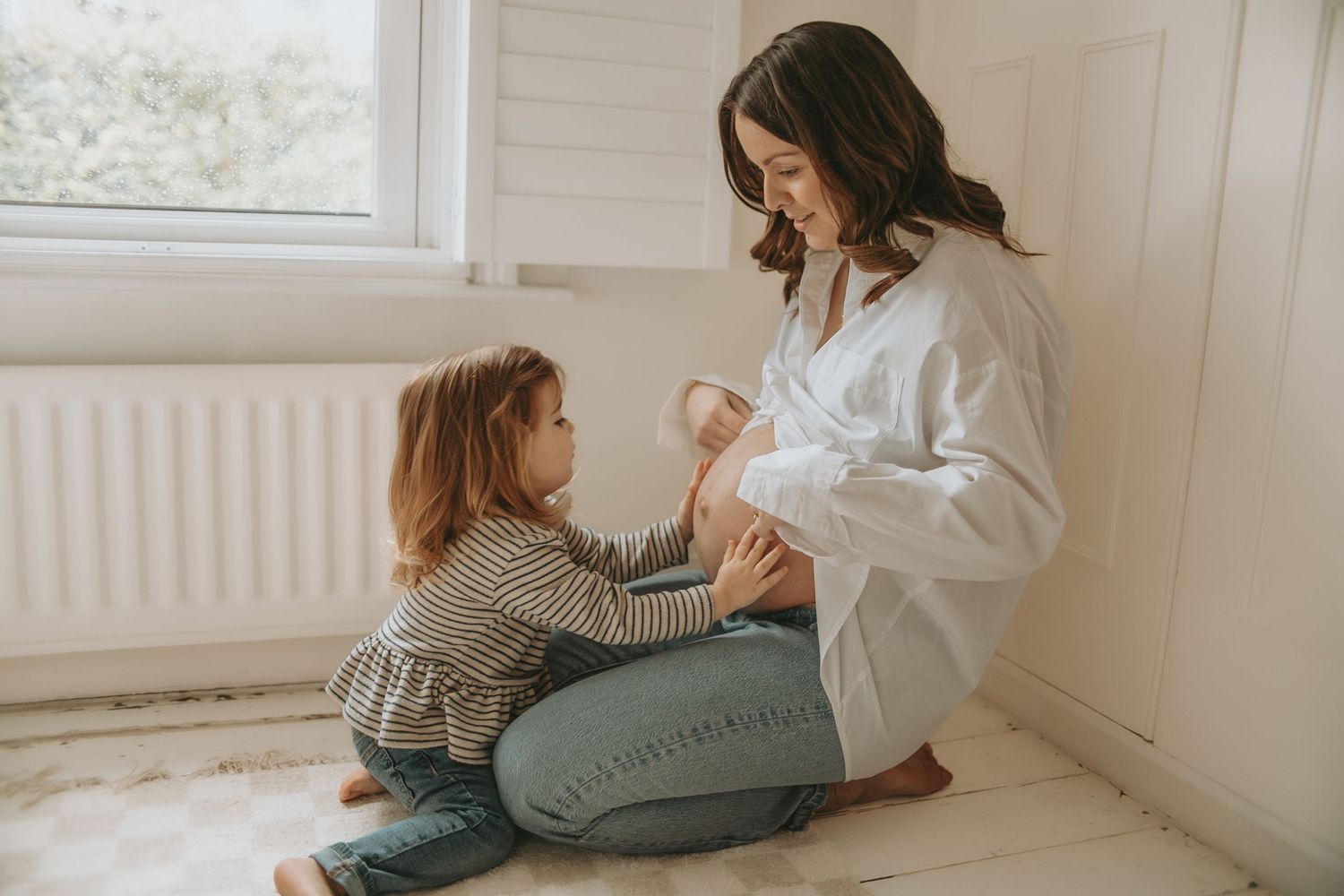 Parent and child sitting together on floor by sunny window.