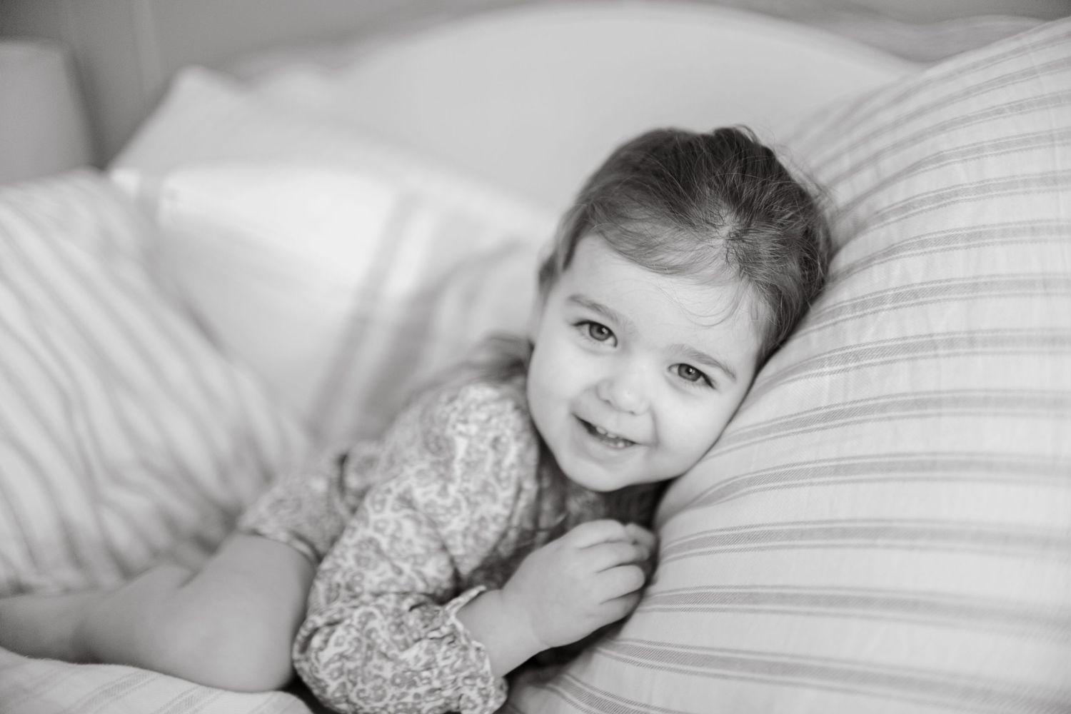 A child smiling while resting on striped pillows in black and white.