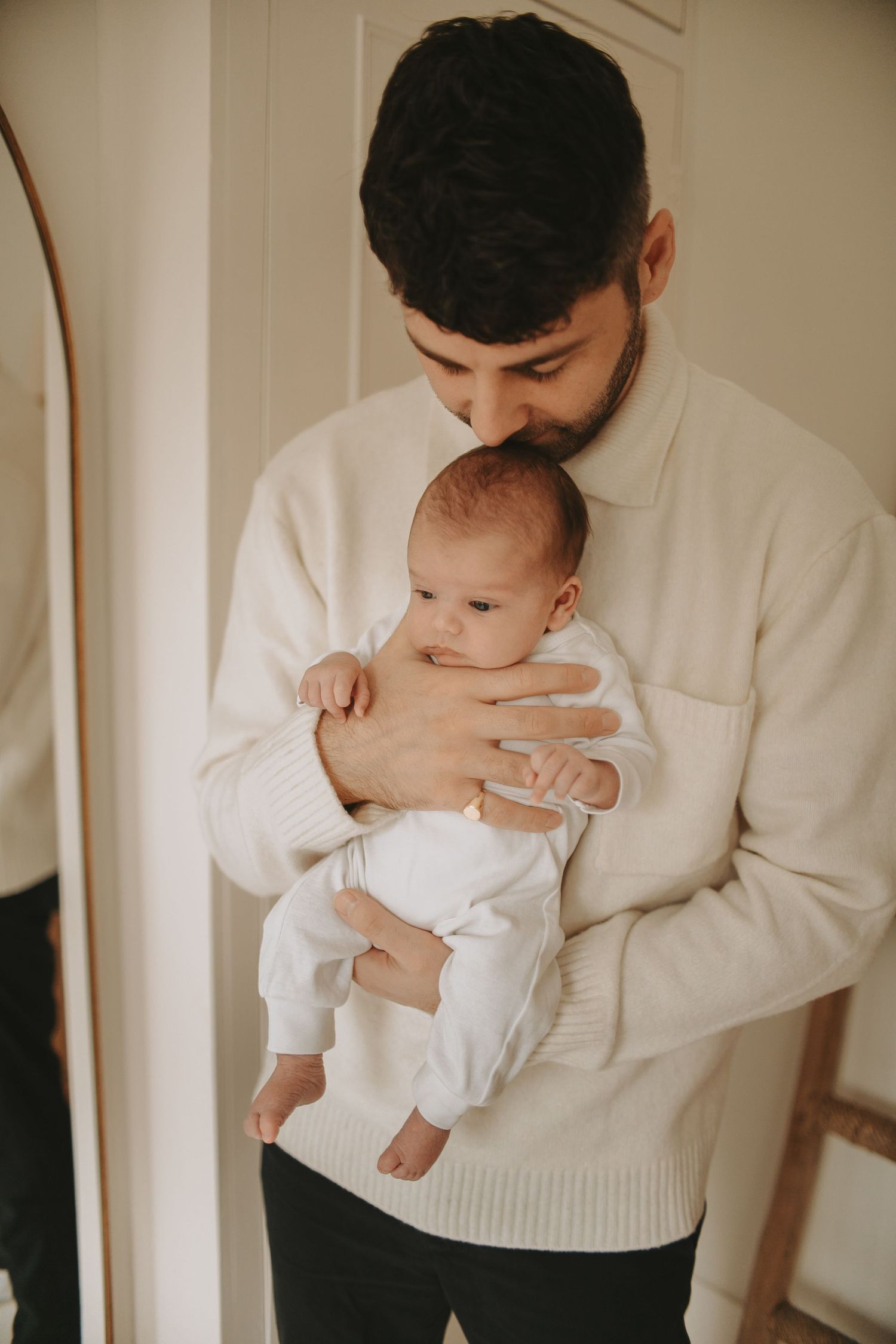 A person in a white sweater holding and looking down at an infant in white clothing.