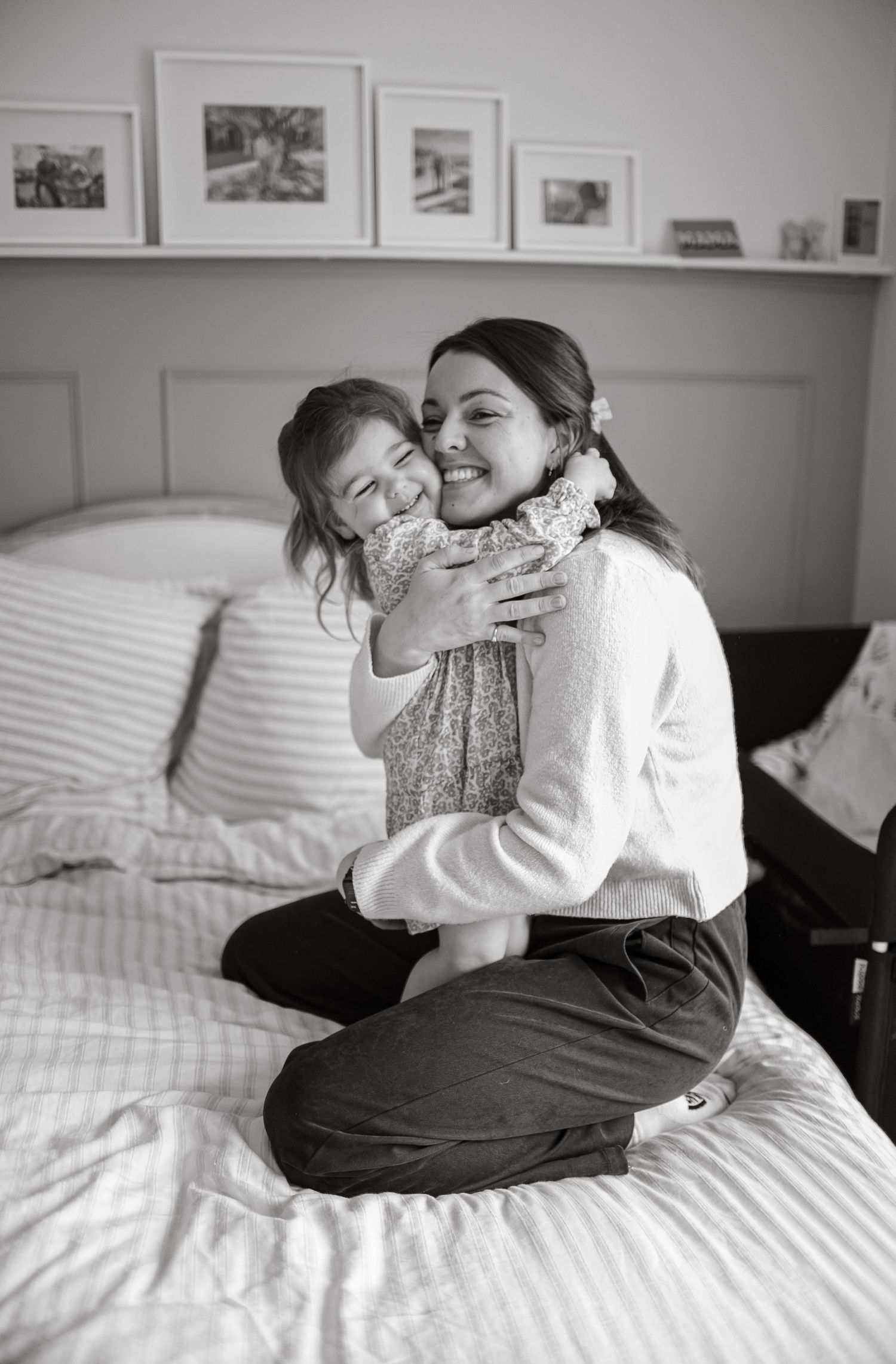 A heartwarming embrace between two people on a bed with framed photos on the wall.