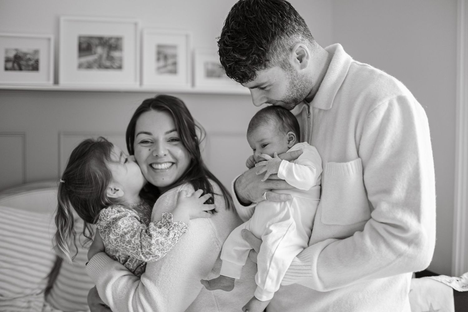A family of four sharing intimate moments and laughter on a bed.