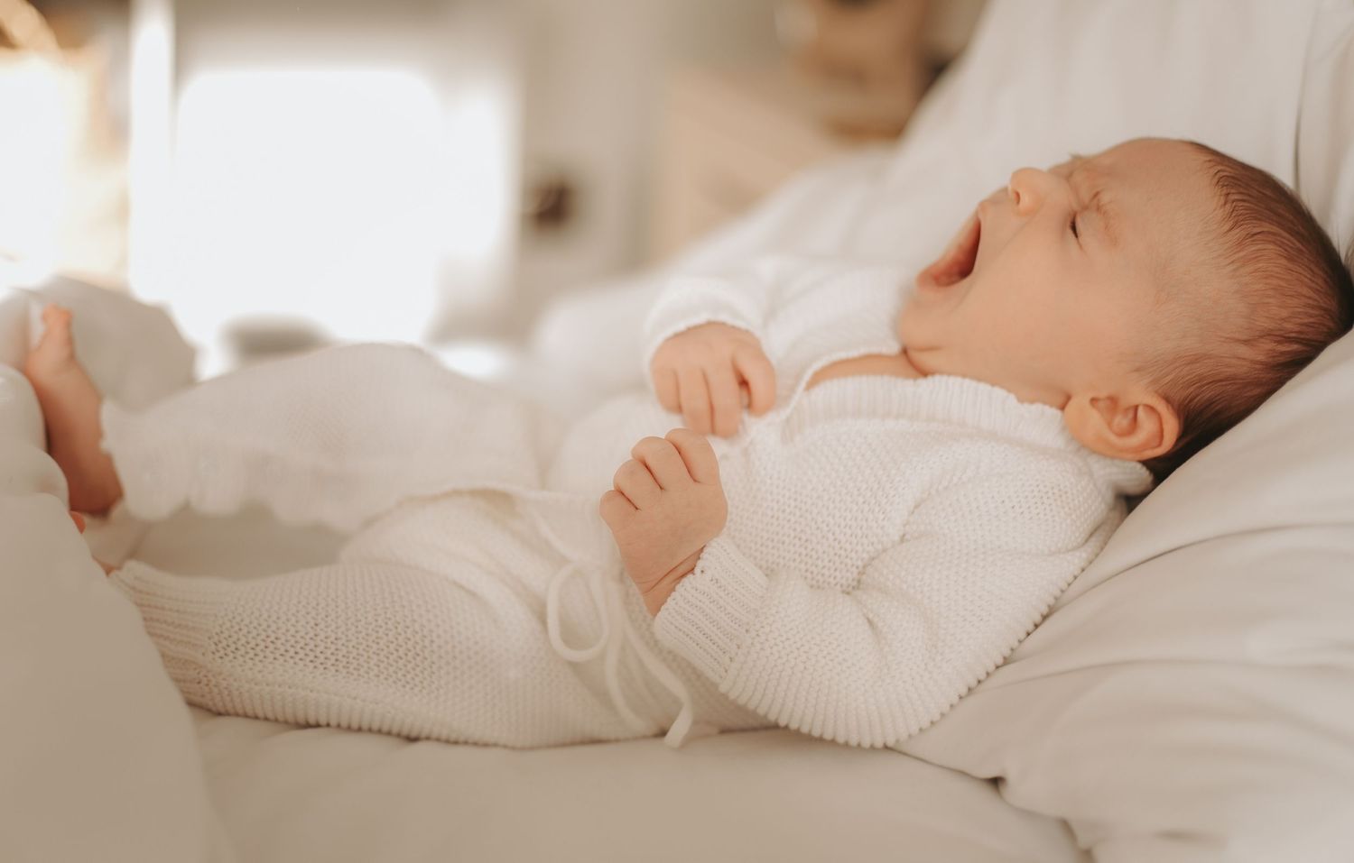 Newborn baby resting peacefully on white bedding during professional photography session.