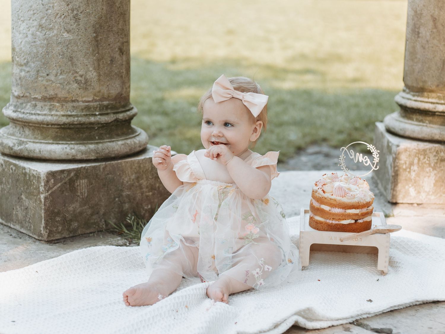 Baby's cake smash photo session set up near classical stone columns outdoors.