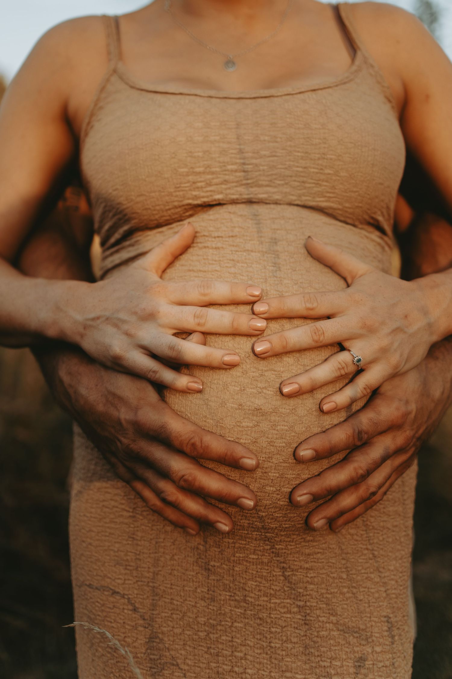 Hands tenderly cradle a pregnant belly wearing a textured beige dress.