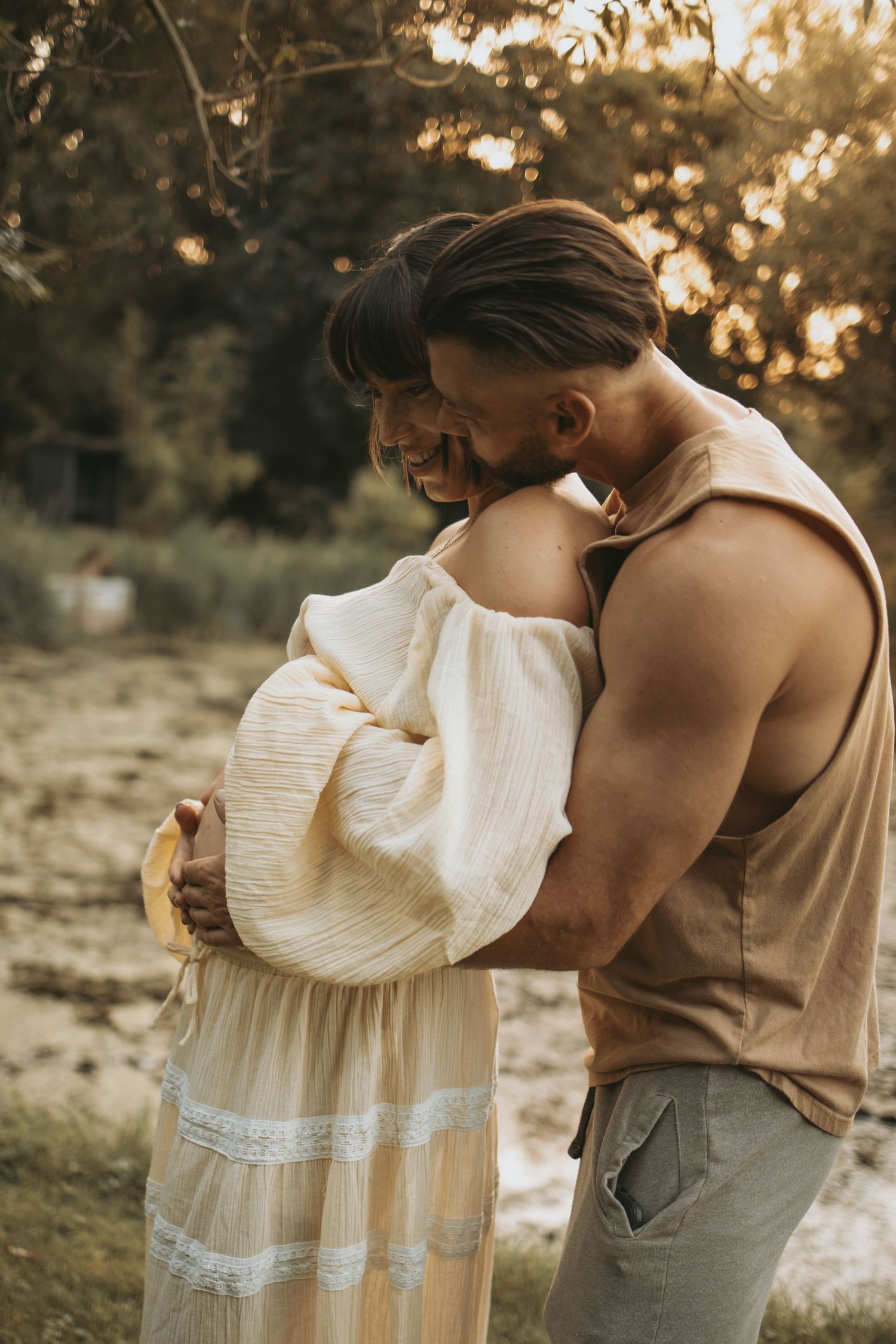 A couple embraces in warm sunlight with the woman wearing a flowing white dress.