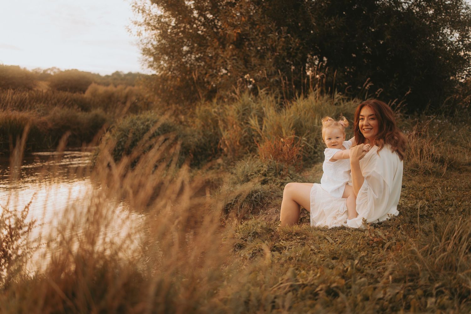 Ethereal golden hour photography session along a peaceful waterfront with natural grasses.