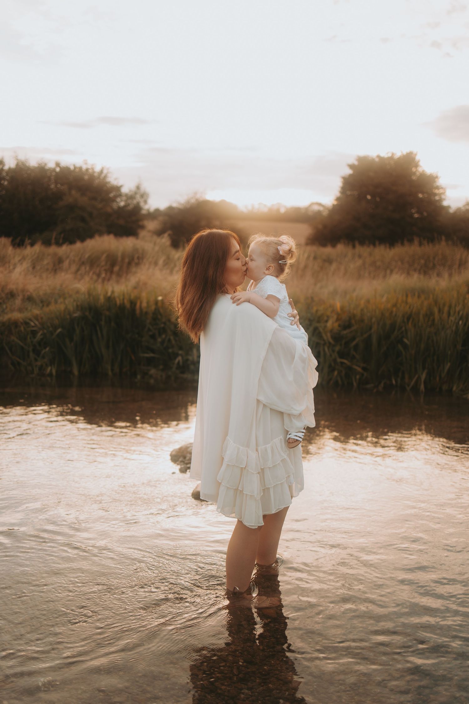 Intimate sunset photoshoot with flowing white dresses in shallow lake waters.