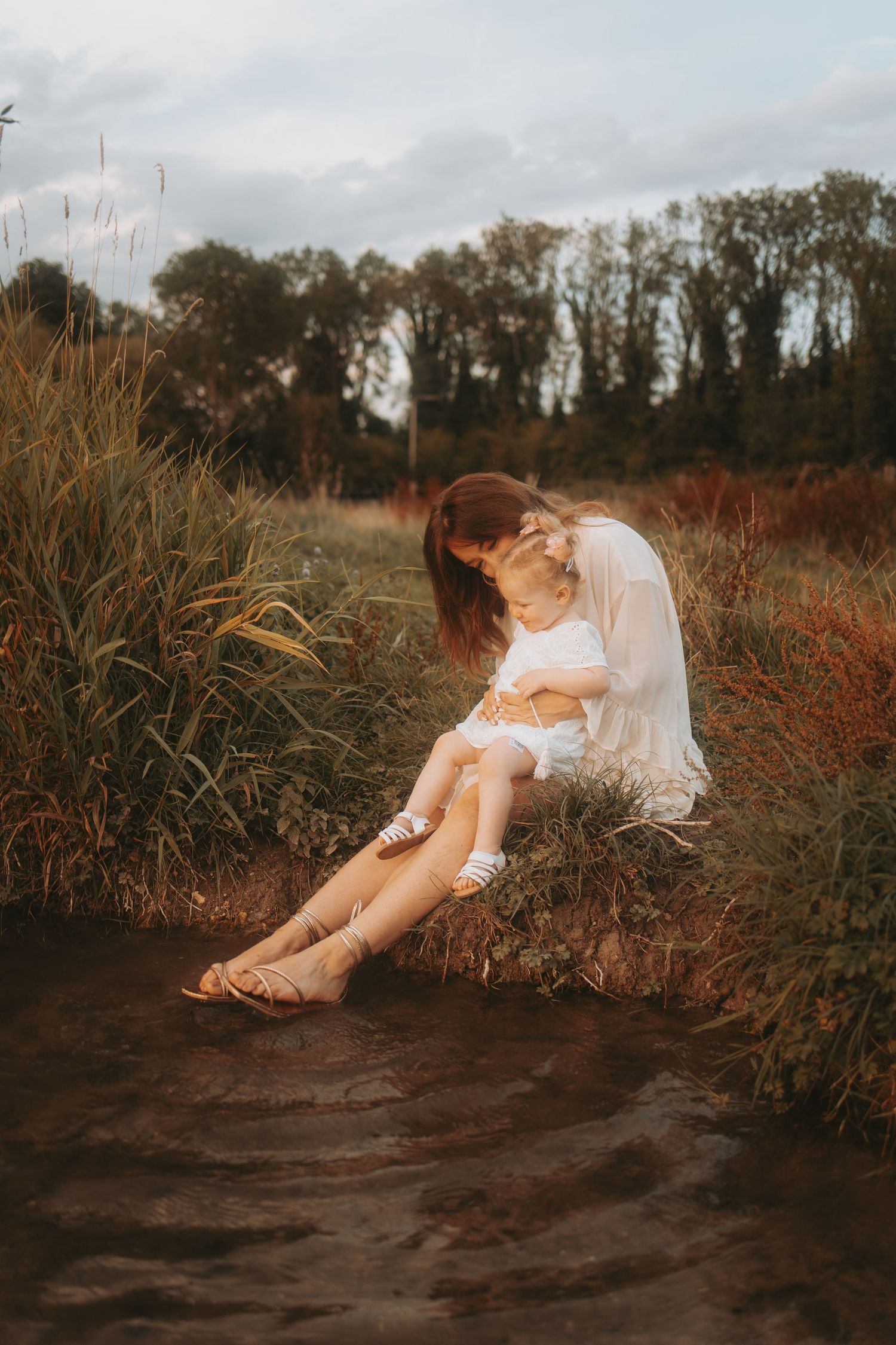 Artistic portrait session on a grassy riverbank during sunset hours.