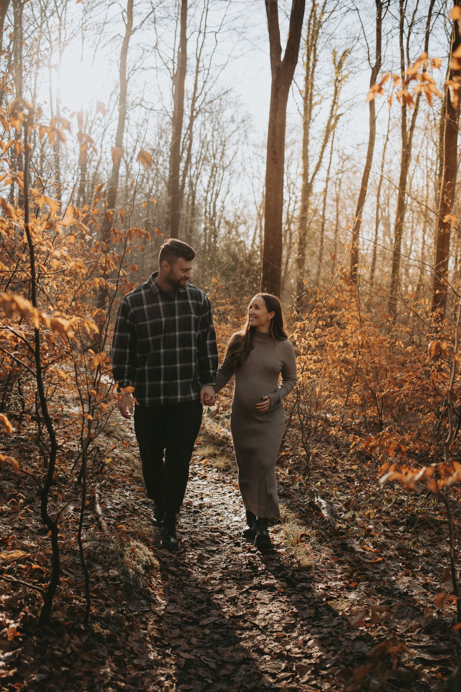 A couple walking through autumn woods with fallen leaves on the ground.