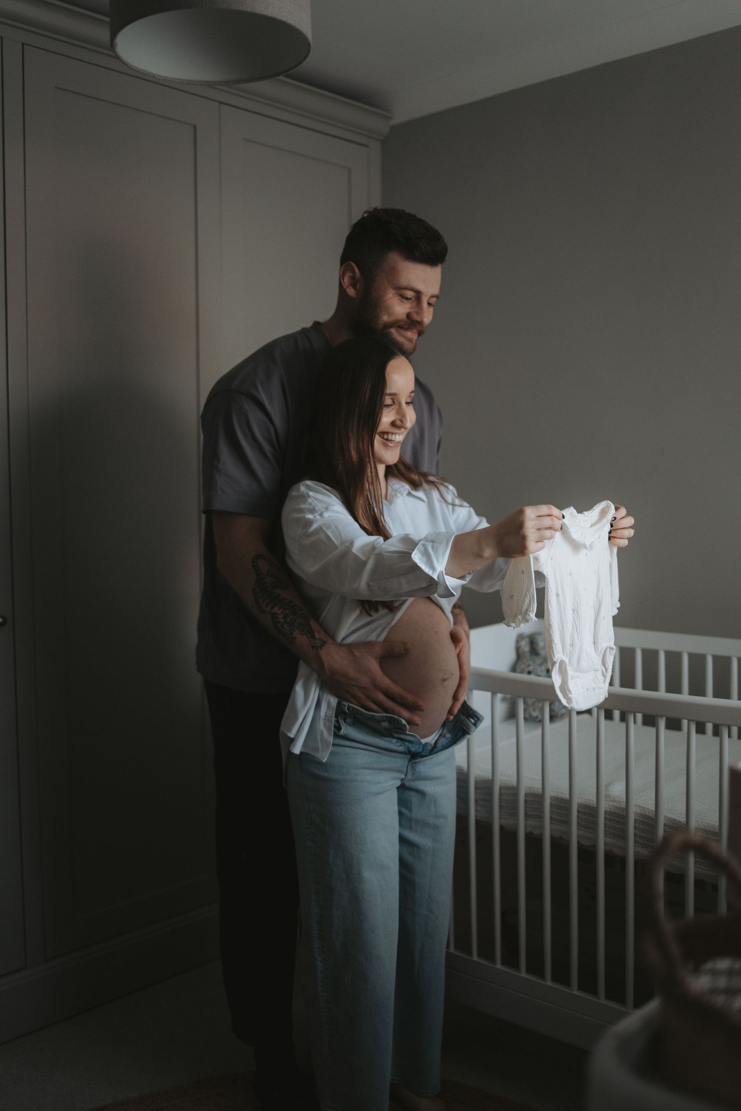 A couple shares an intimate moment in a nursery room with a white crib.