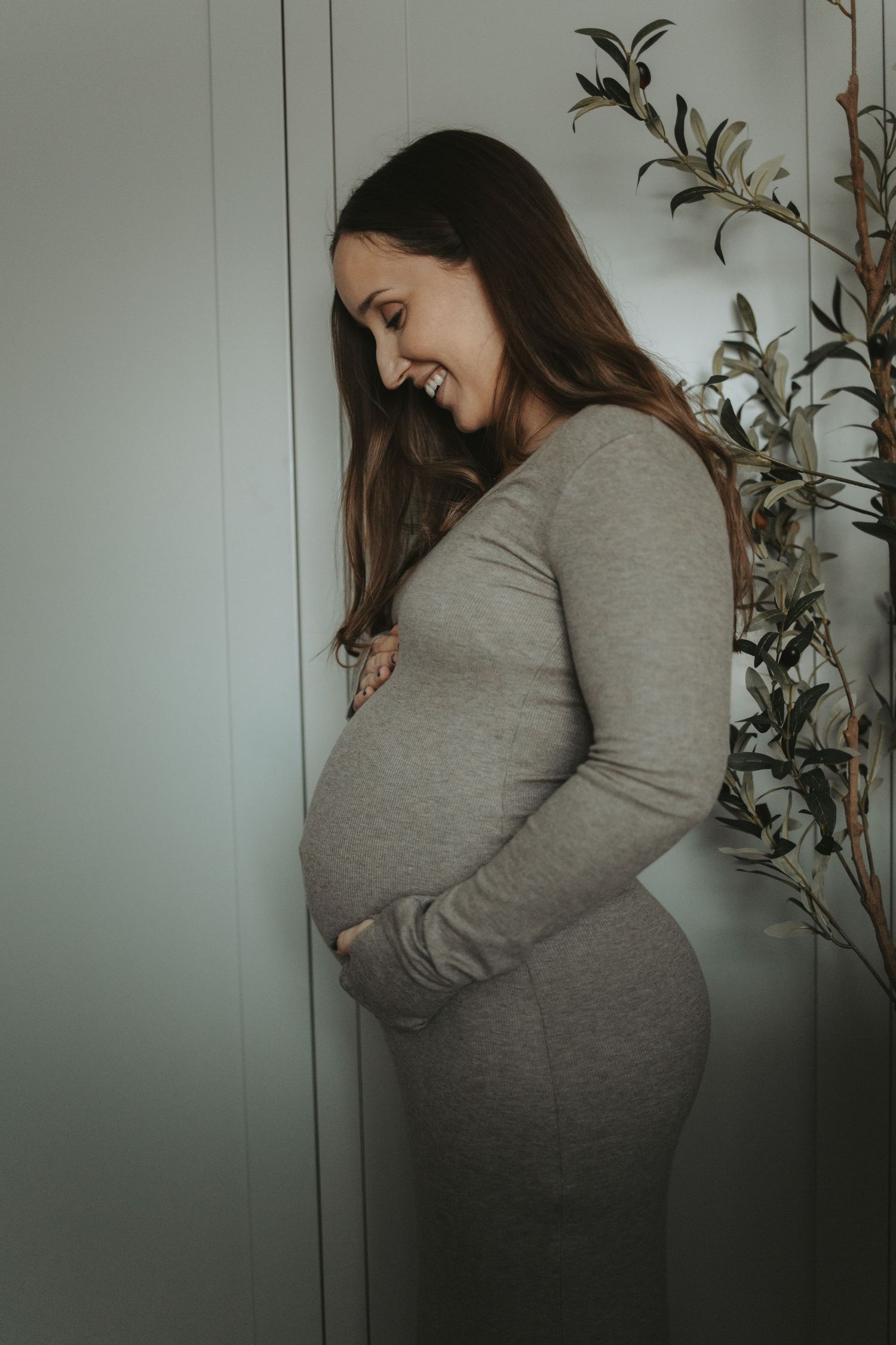 Side profile of an expectant mother in a grey sweater against a light wall.