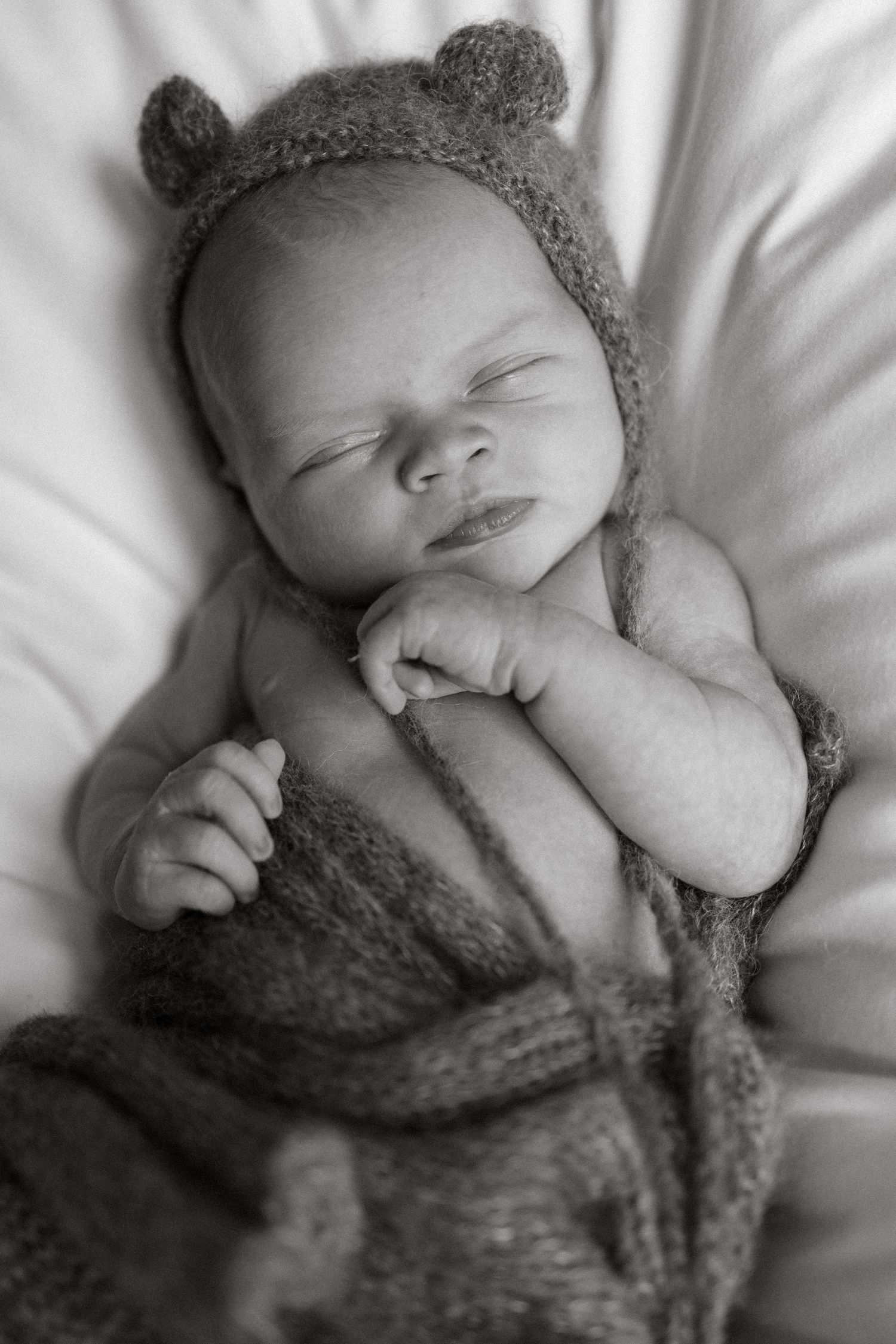 Black and white portrait of sleeping newborn in knit bear hat and wrap.