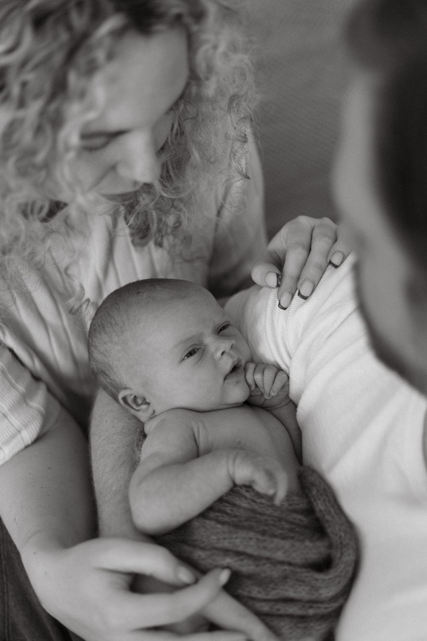 Black and white intimate newborn photography session showing tender moments with baby wrapped in knit blanket.