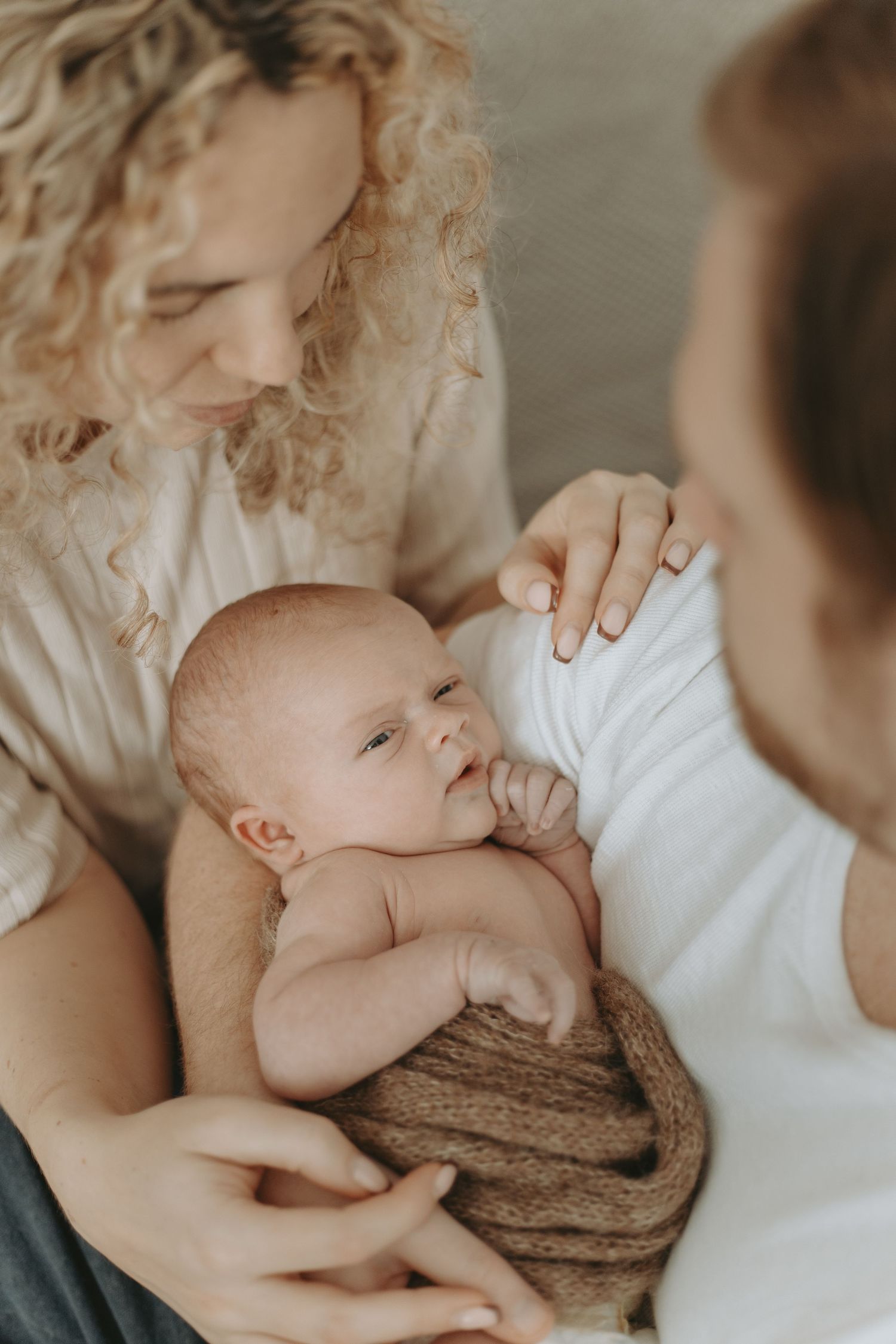 Gentle newborn photography session with baby swaddled in brown knit wrap against neutral background.