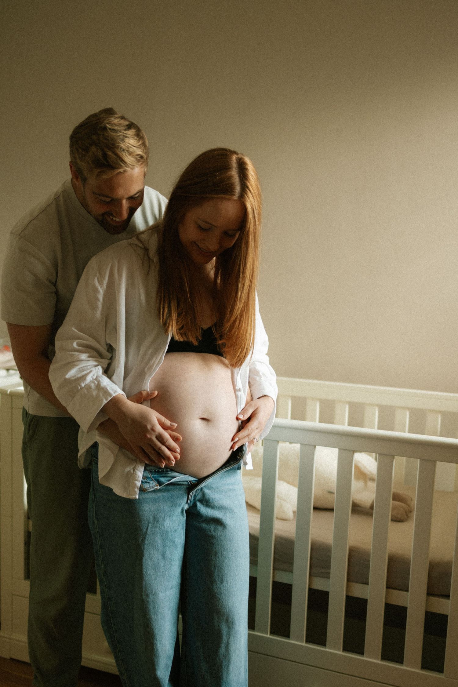 Intimate maternity photoshoot showing couple embracing near white nursery railing.