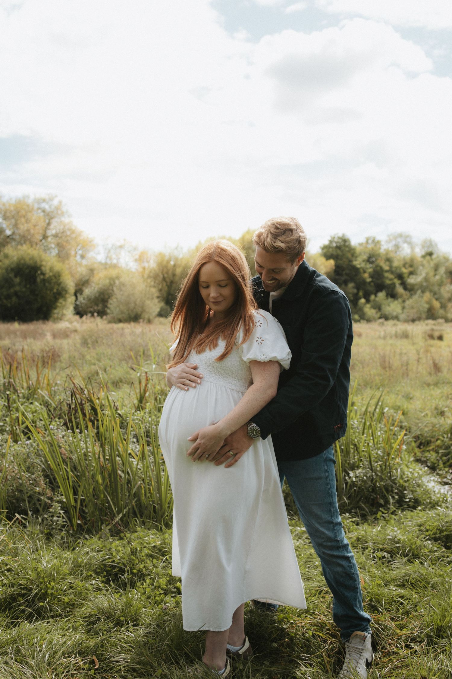 Expecting couple shares tender moments in sunlit meadow during outdoor maternity shoot.
