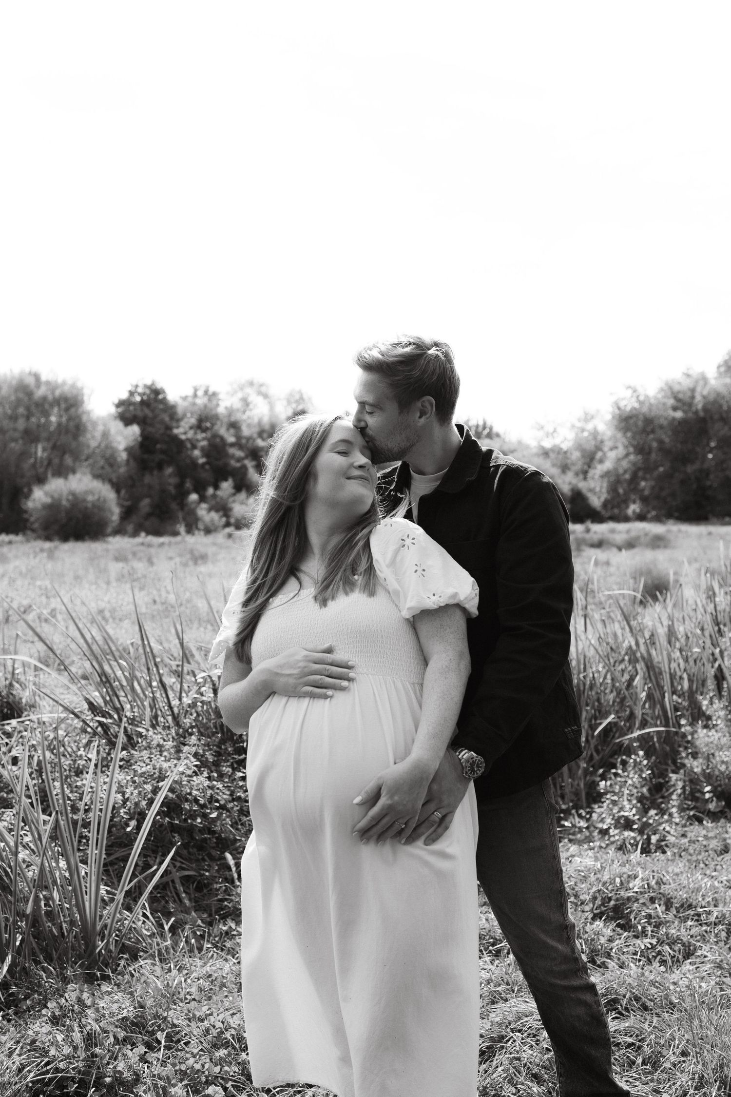 Black and white maternity portraits of couple embracing in natural outdoor setting.