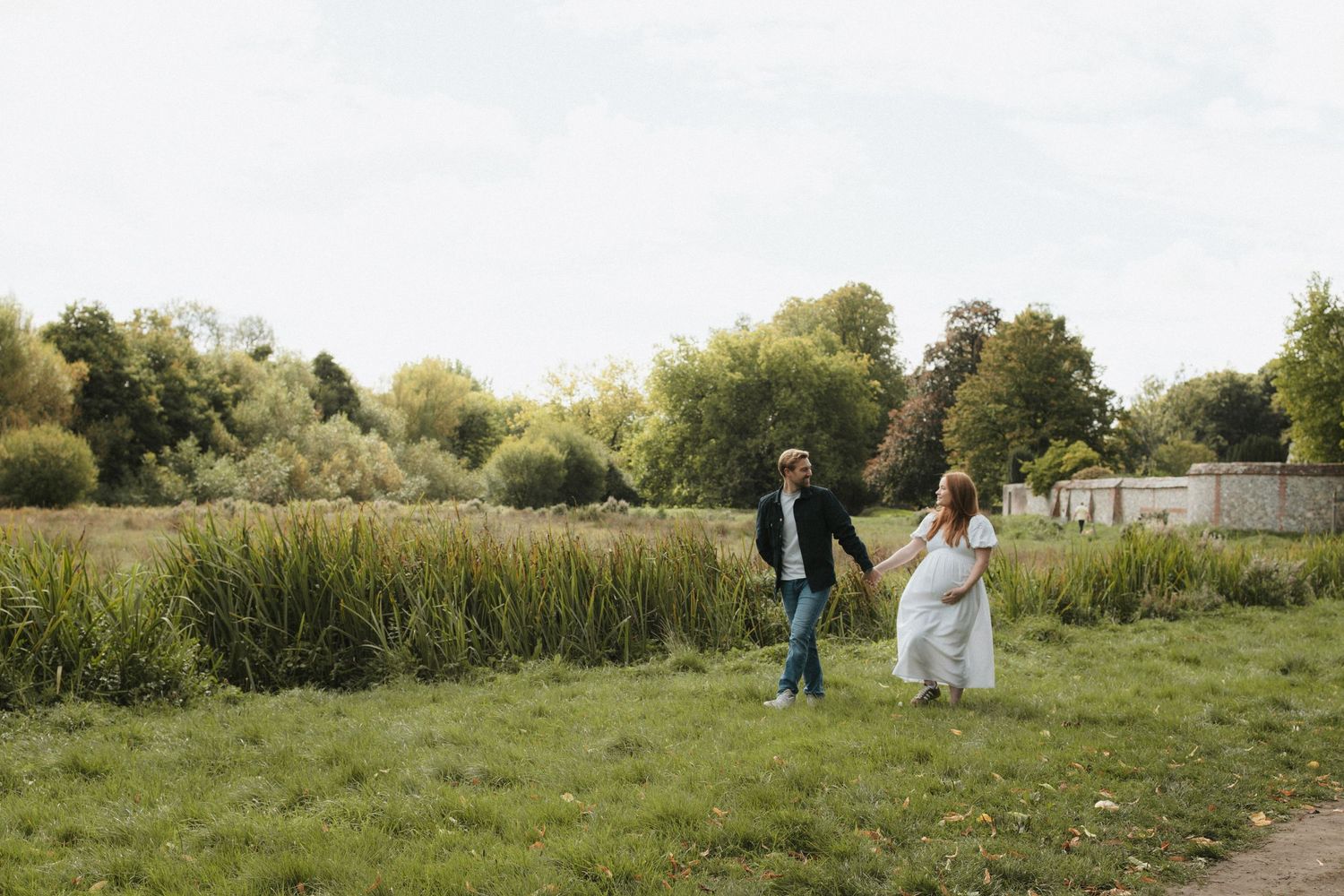 Couple walking together through a scenic grassy meadow at sunset.
