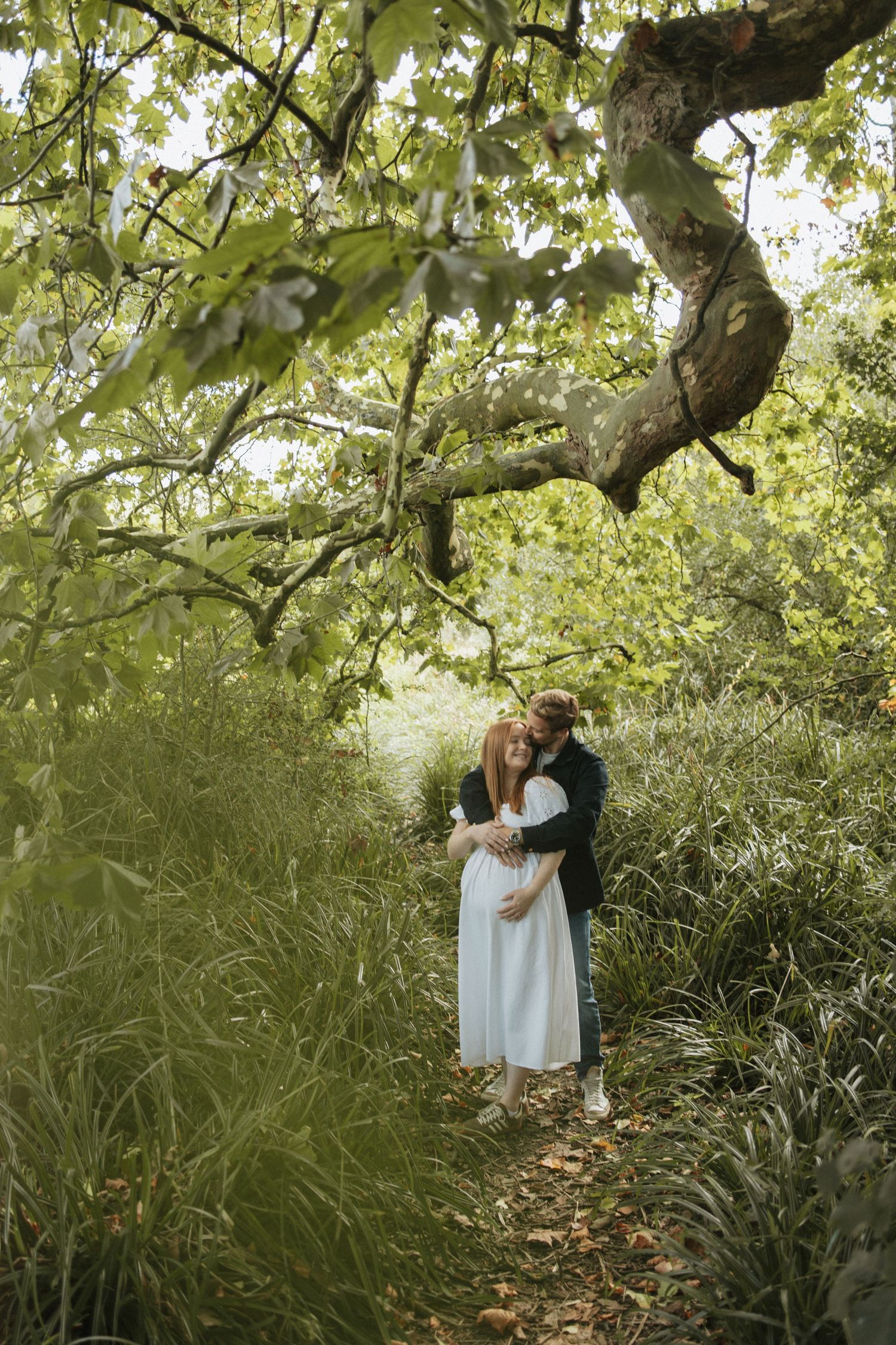 Romantic moment under a large tree with green foliage and natural lighting.