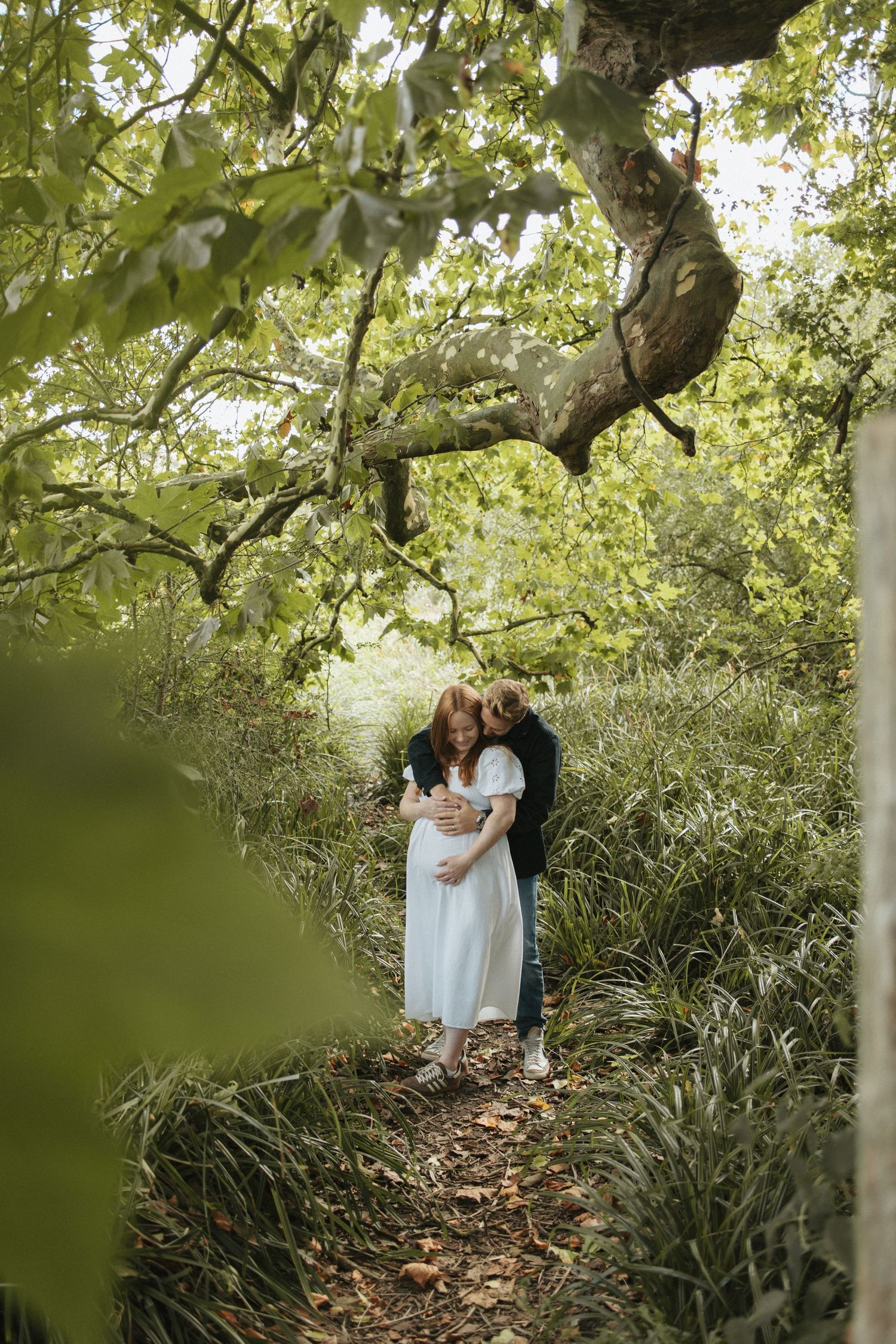 Intimate outdoor photoshoot beneath sprawling tree branches in natural setting.