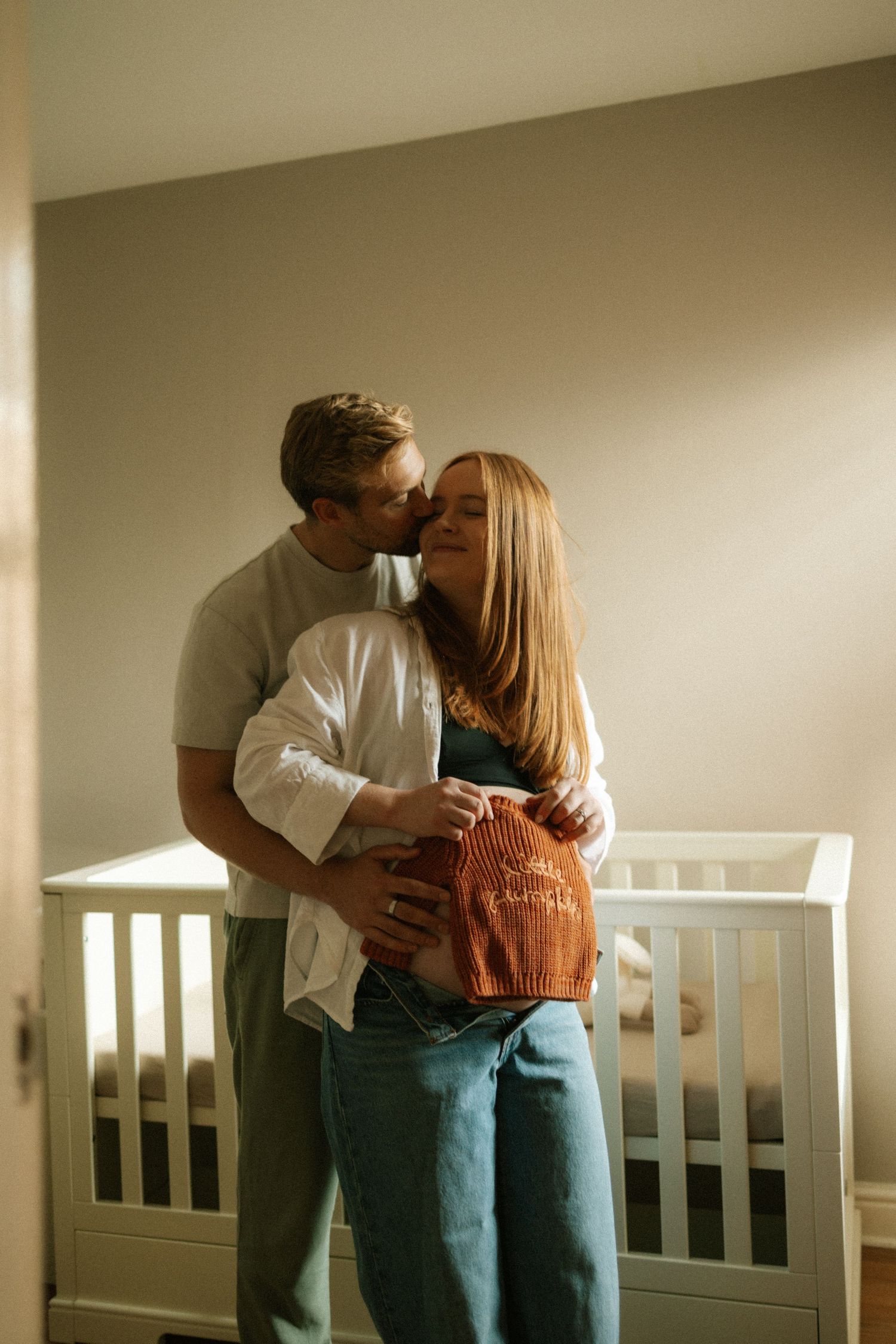 Tender moments captured between expectant couple in casual attire by nursery furniture.