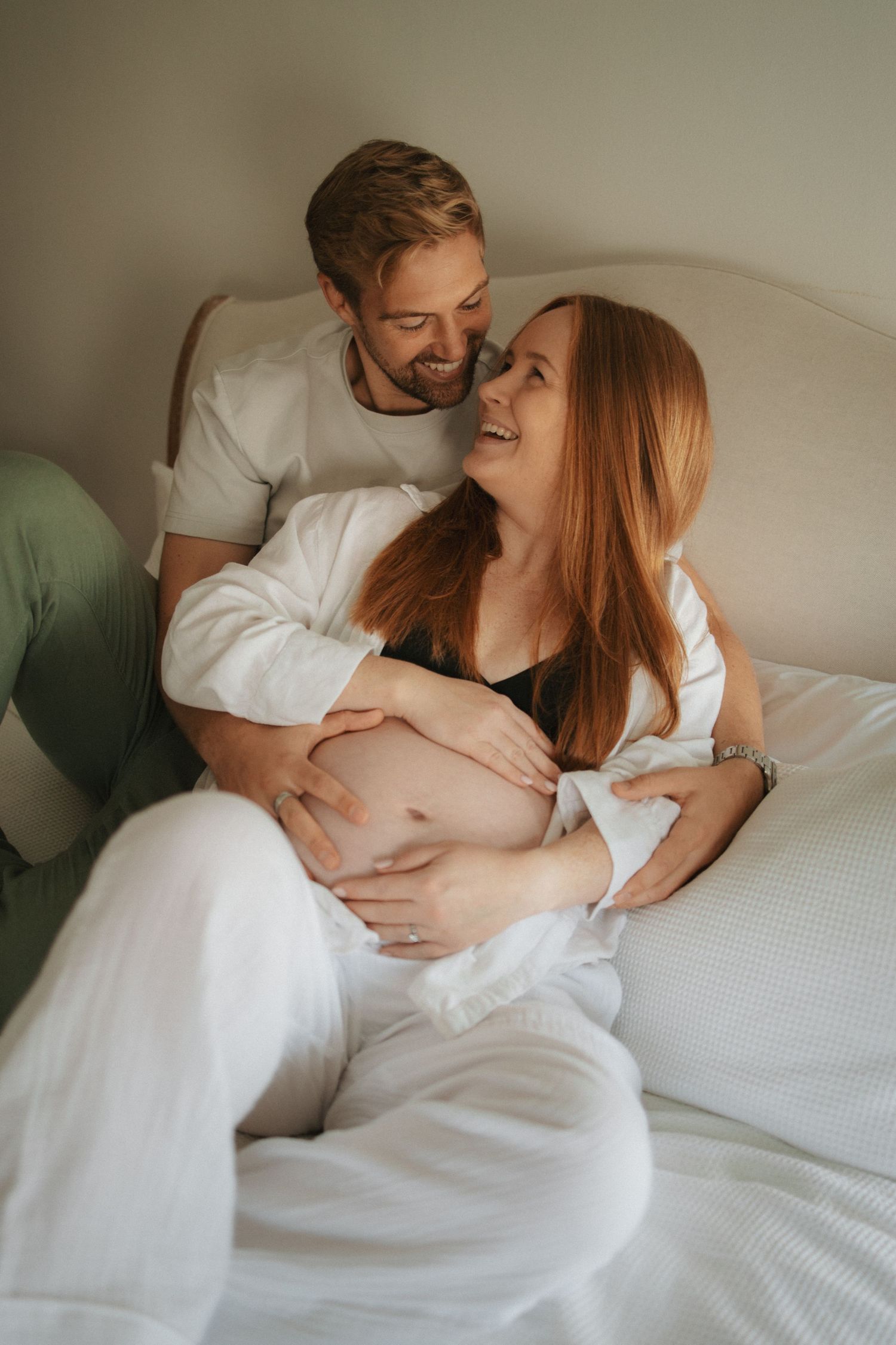 Intimate maternity photos of couple sharing loving moments on white bedding.