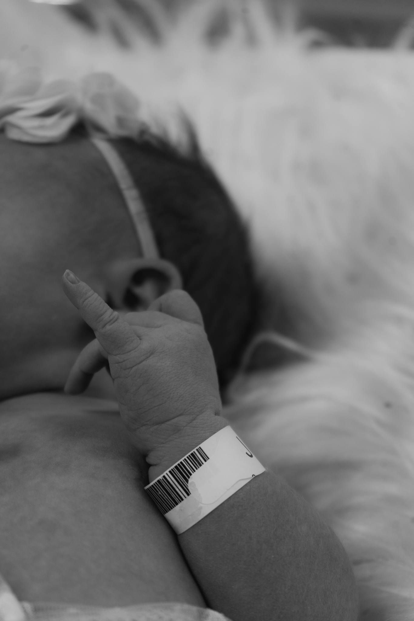 Black and white close-up of a newborn's tiny hand wearing a hospital identification bracelet.