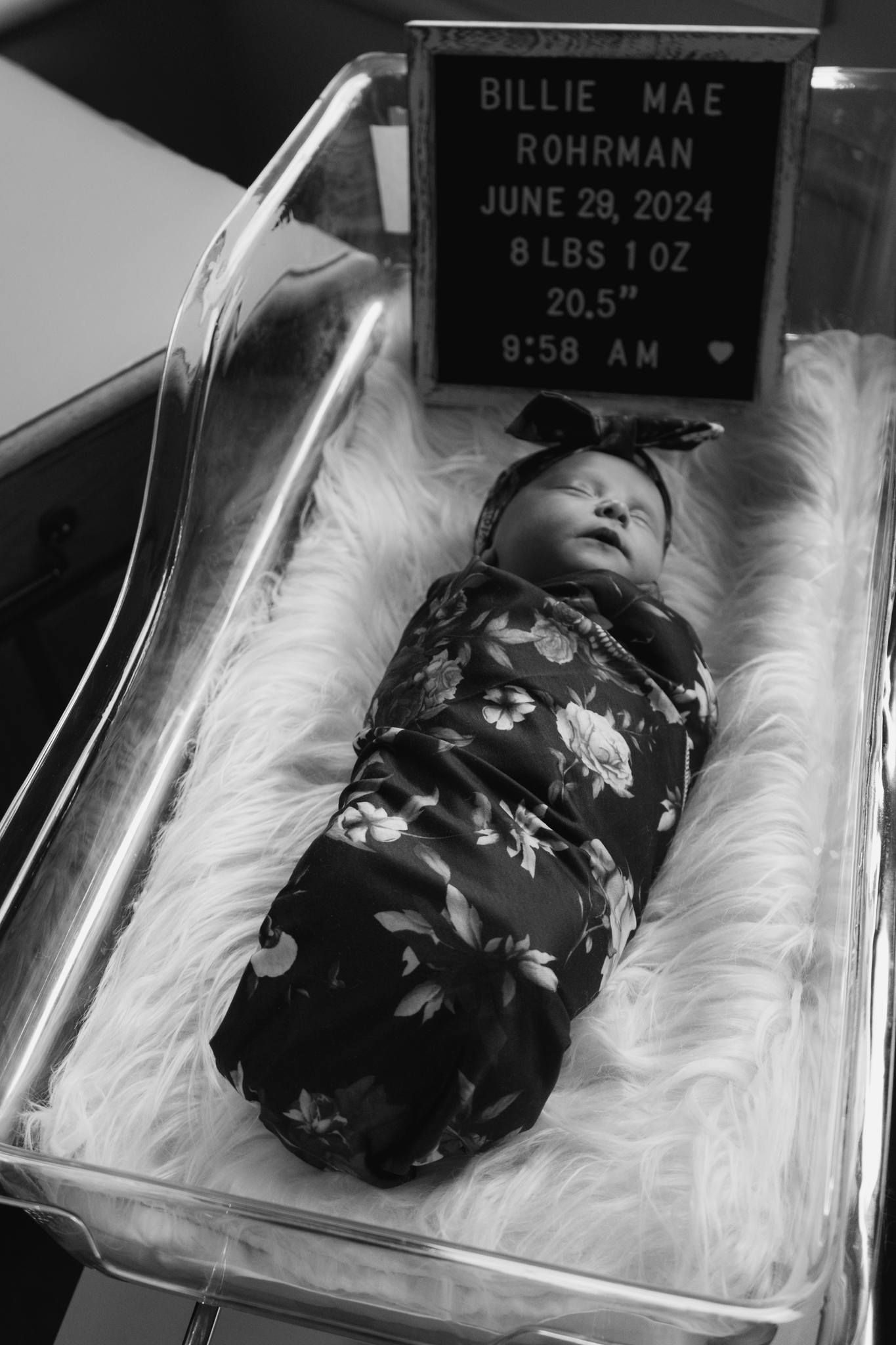 Swaddled newborn girl Billie Mae Rohrman in hospital bassinet with birth announcement sign.