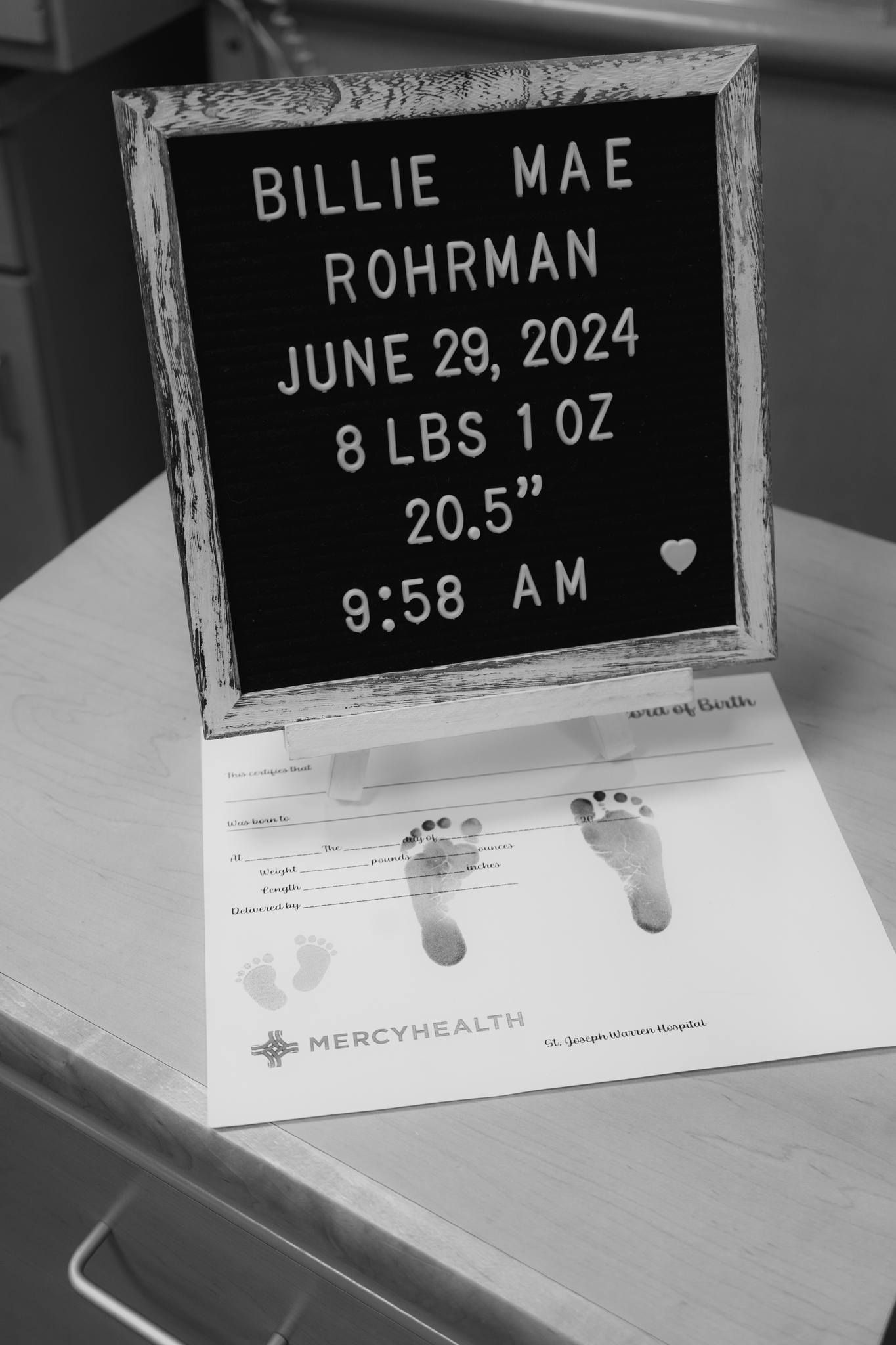 Black letter board announces Billie Mae Rohrman birth stats June 29 2024 8lbs 1oz with newborn footprints below.
