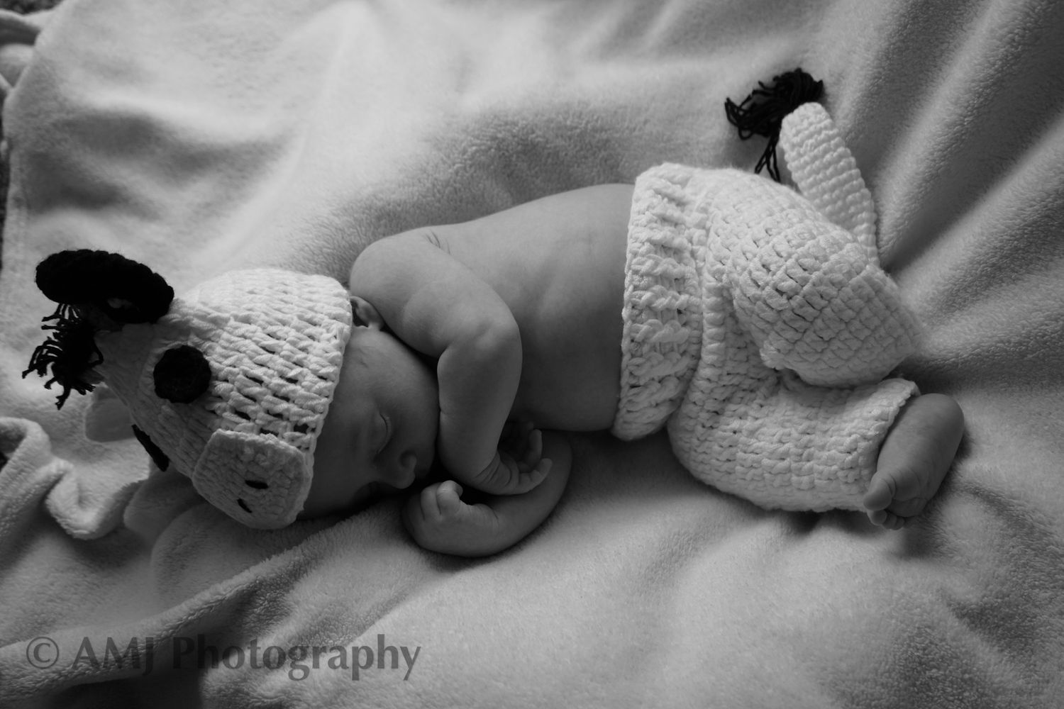 Sleeping newborn baby in crocheted white puppy outfit lying on soft white blanket.