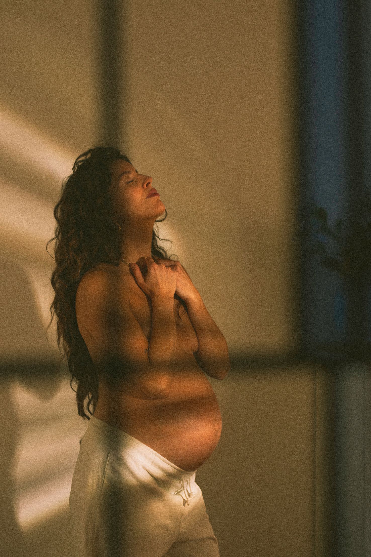 Artistic portrait with golden hour lighting through window creating dramatic shadows.