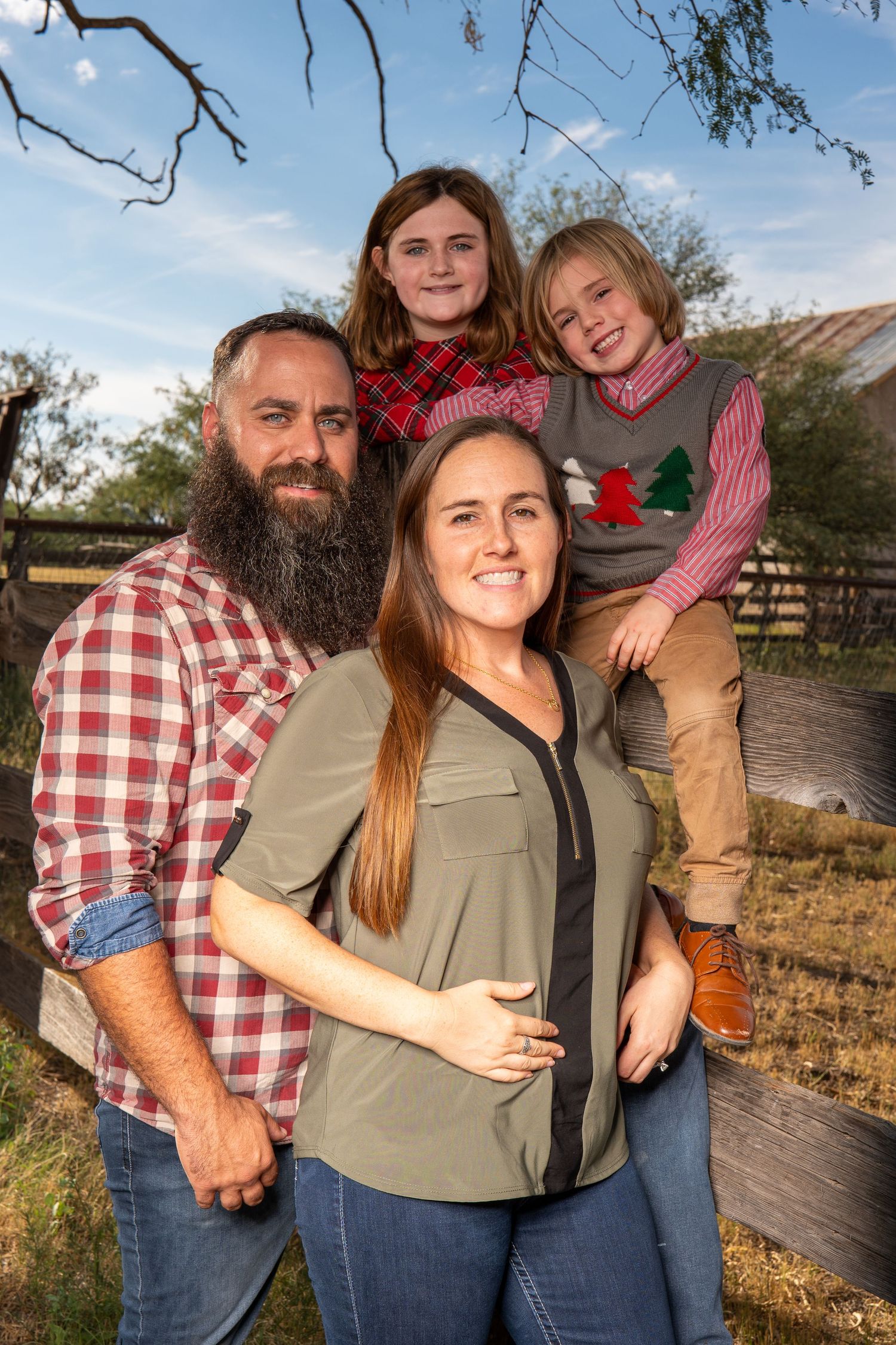 Family portrait in casual western wear standing together against a ranch backdrop.