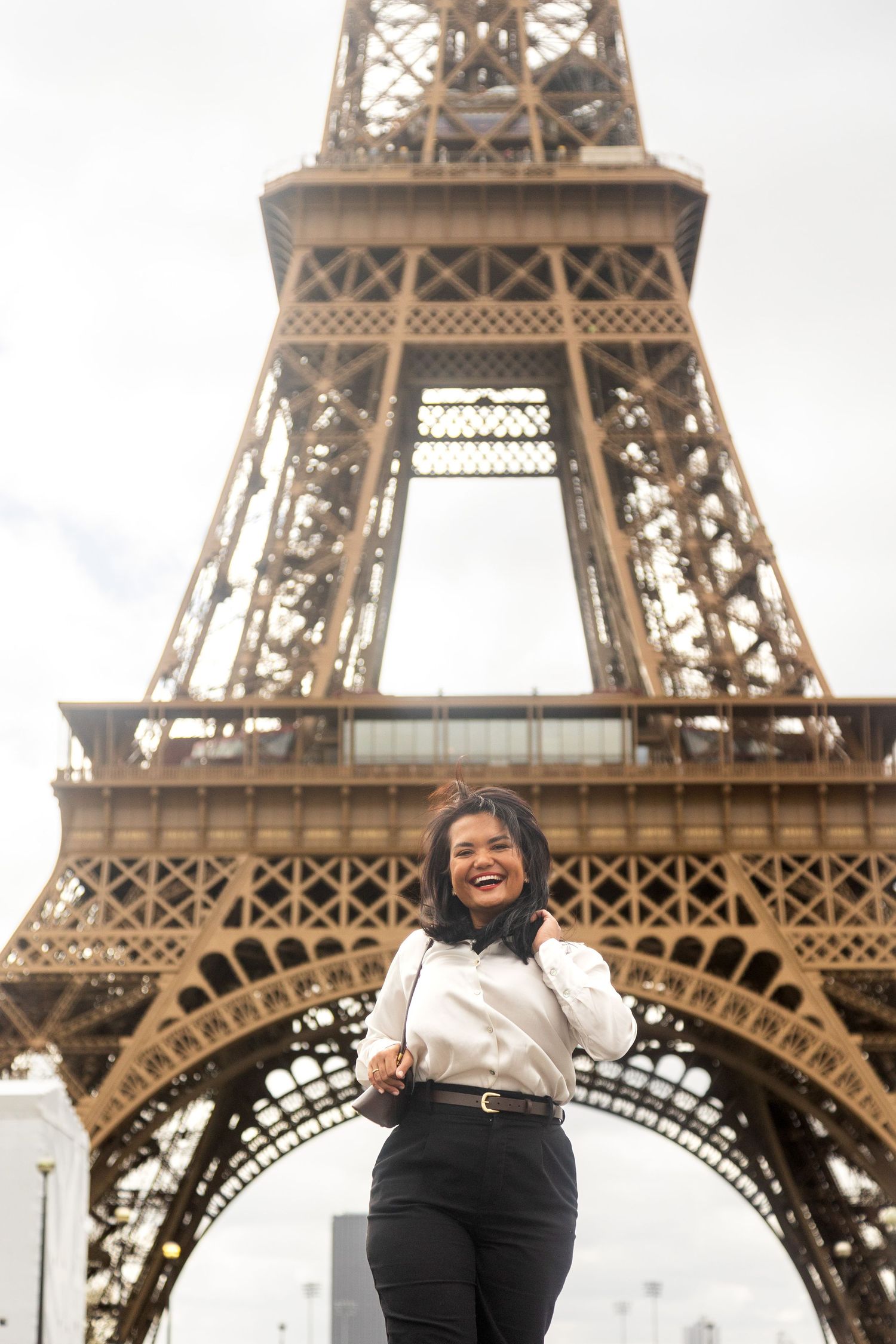 A stylish visitor poses in front of the majestic Eiffel Tower on a cloudy day.