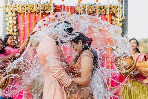Couple kissing during a joyful water splash ceremony at a colorful Indian wedding celebration.
