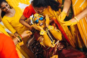 Festive Indian pre-wedding celebration with participants in yellow and red traditional attire.