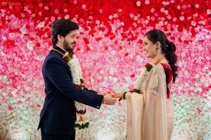 Couple exchanging garlands at a vibrant Indian wedding ceremony with a stunning red and pink floral backdrop.