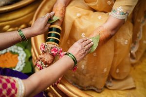Close-up of Indian bride's henna hands during traditional wedding ceremony with gold saree and green bangles.