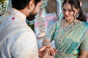 Indian bride in teal saree and groom exchange rings at traditional wedding ceremony.
