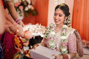 Smiling Indian bride in pink saree and floral garland receiving ritual offerings during traditional wedding ceremony.