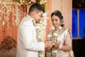 Indian bride and groom exchanging rings during traditional wedding ceremony, adorned in elegant attire and floral garlands.
