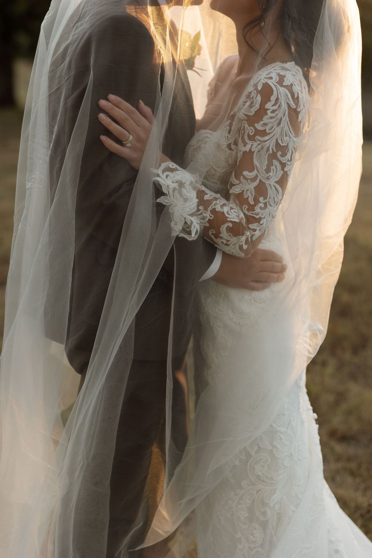 Couple in formal wedding attire by a white luxury car outside a modern white building.