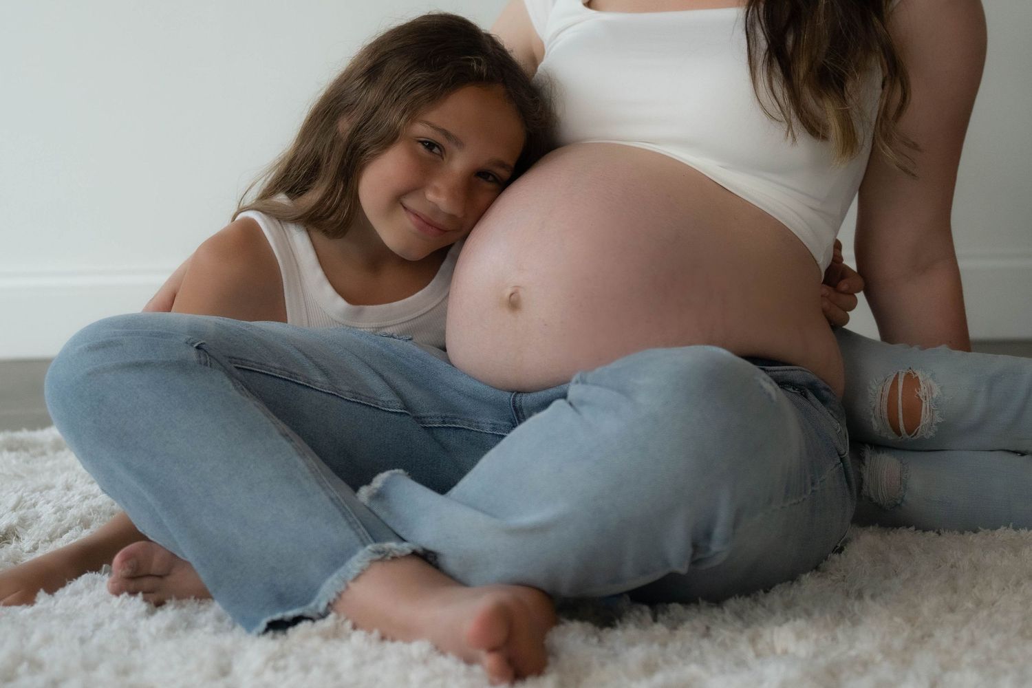 Candid maternity moments captured on plush white carpet in natural light.