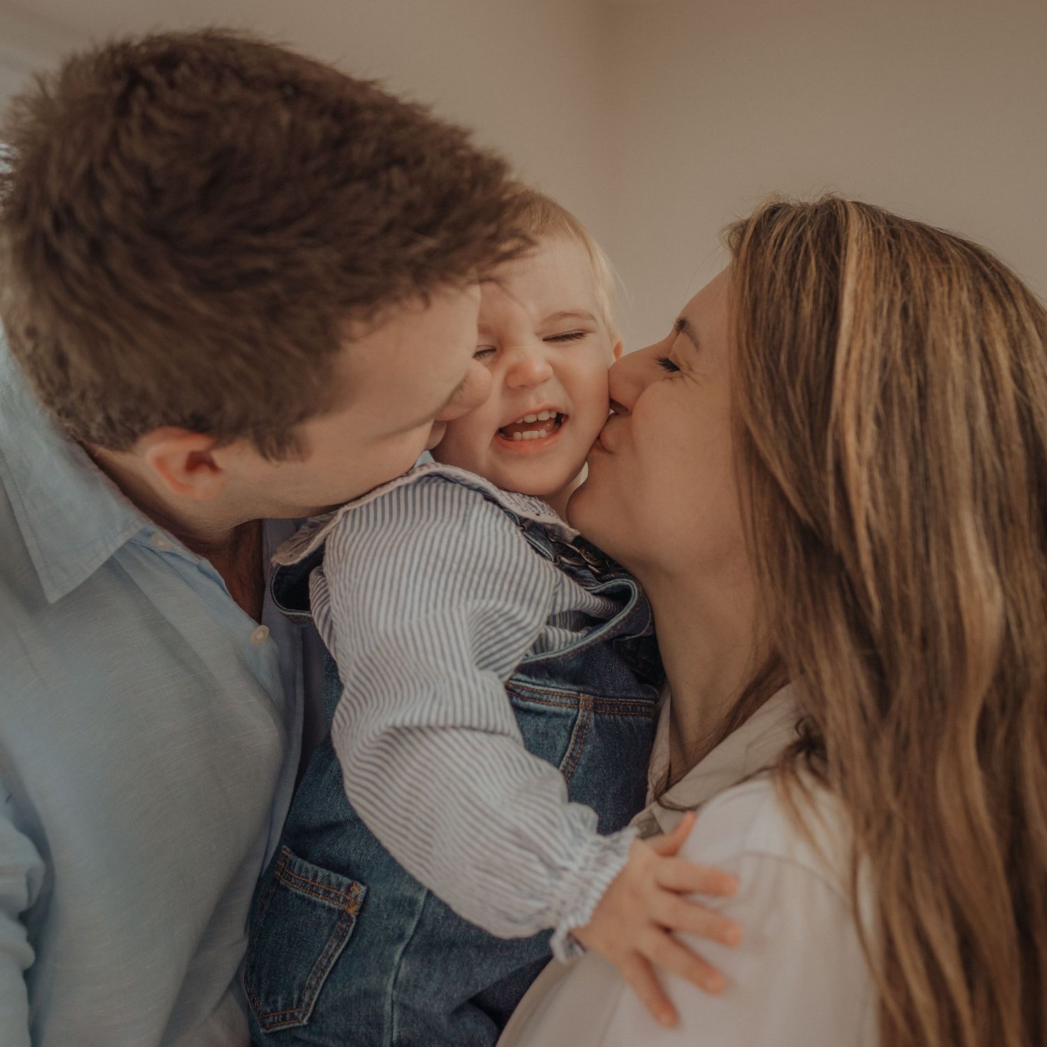 Intimate family moment as parents kiss their laughing baby.