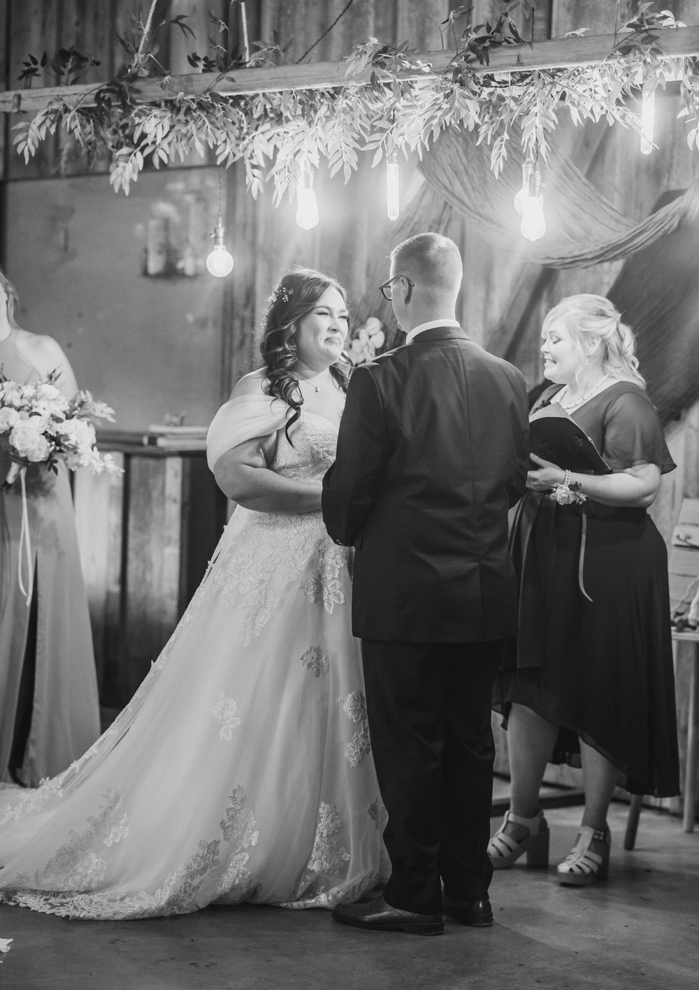 Black and white photo of bride and groom exchanging vows at rustic barn wedding ceremony.