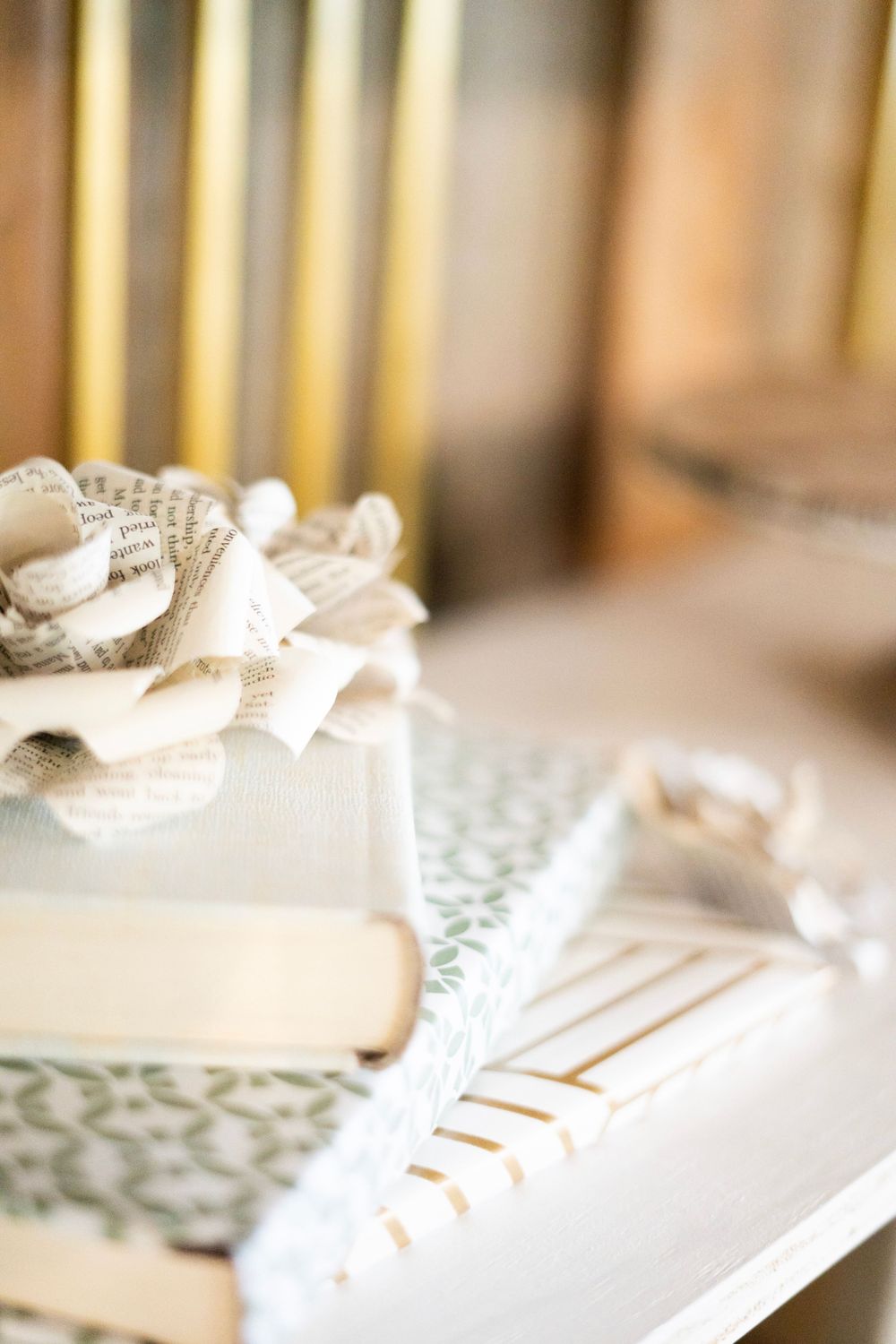 Decorative gift box with book page bow on patterned surface with gold striped pens at a wedding reception table.