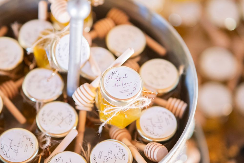 Rustic honey jar wedding favors with wooden dippers and personalized tags displayed in a bucket.